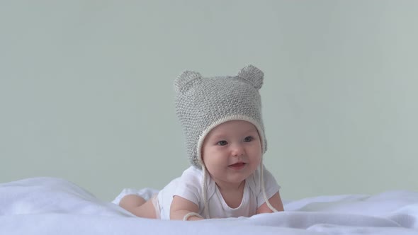 Happy baby girl  in hat laying on the bed and laughs