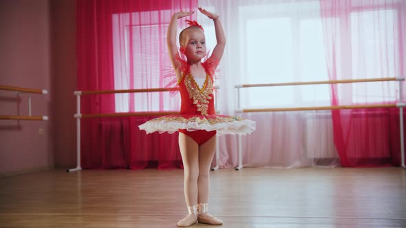 A Little Girl in Red Dress Stands in Ballet Position