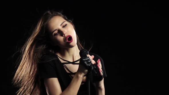 Singer Holds a Microphone Stand in Her Hands, Her Hair Develops in the Wind. Black Background. Slow