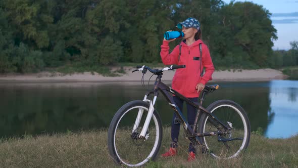 Girl with a bicycle on the nature drinks water.