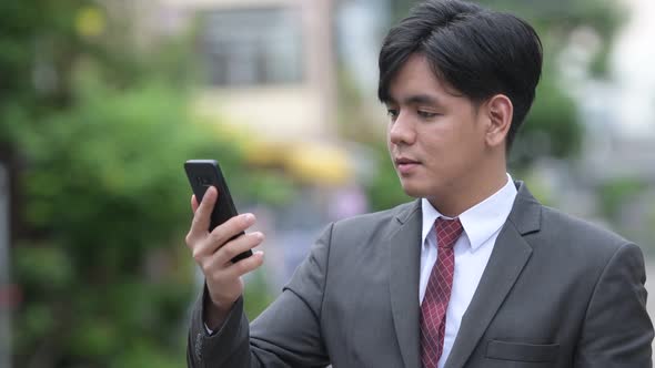 Young Handsome Asian Businessman Using Phone in the Streets Outdoors