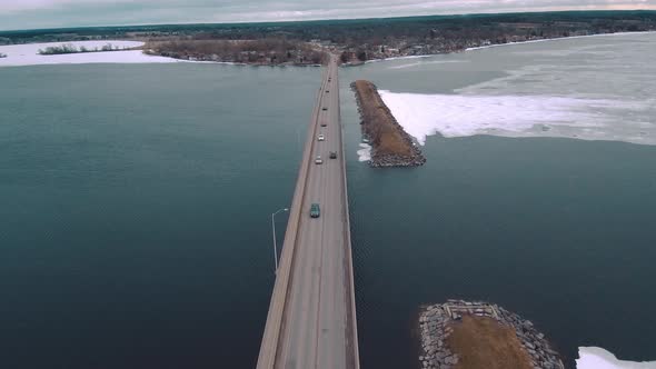 4K Aerial Shot of Cars Driving Over Icy Water on a Huge Highway Bridge Surrounded by a Large Frozen