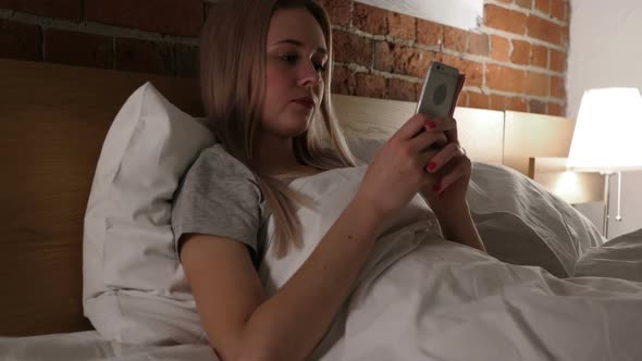 Woman in Bed Browsing Scrolling on Smartphone at Night