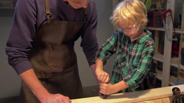 Boy Fixes the Board on the Table in the Workshop