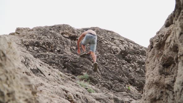 Athletic Guy Naked To the Torso Climbs Up the Rock. Slow Motion. Lower Angle.