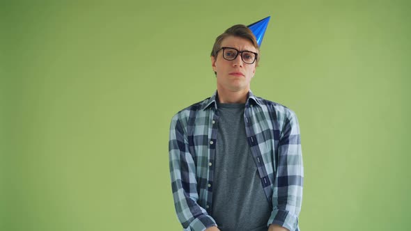 Portrait of Unhappy Young Man in Party Hat Looking at Camera with Sad Face