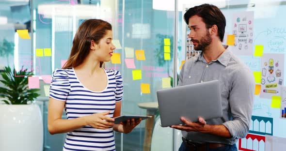 Male and female executives discussing over electronic devices