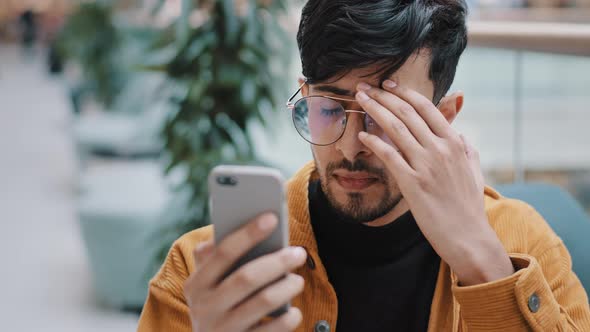 Closeup Young Sad Unhappy Arab Man Looking at Phone Screen Reading Email Being Shocked By Terrible