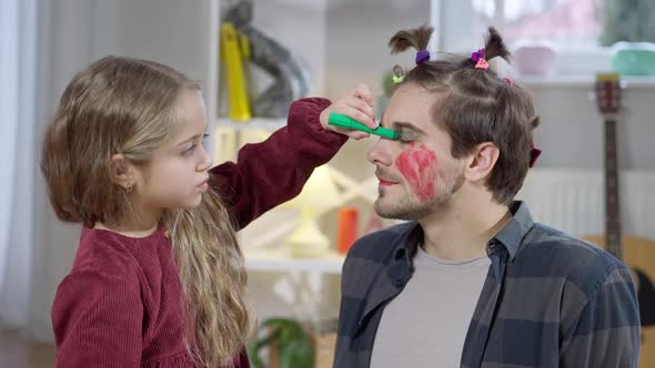 Happy Daughter Painting Father Face with Multicolored Markers Looking at Camera and Smiling