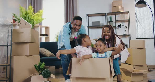 African American Couple Playing with Their Two Funny Daughters which Climbing Inside into Carton Box