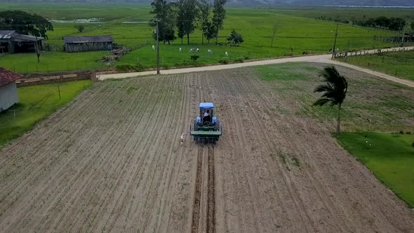 High aerial shot slowly following a tractor cultivating a farmer's field in the evening with two dog