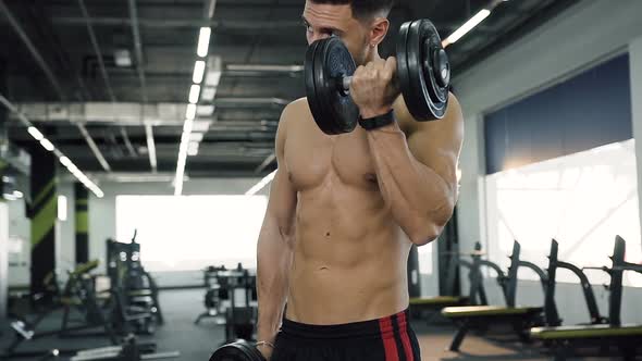 Handsome Fit Man without t-shirt Making Exercises for Hands with Dumbbells.