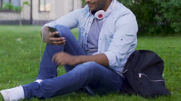 Mixed-Race Guy Sitting on Grass With Mobile Phone and Headphones, Application