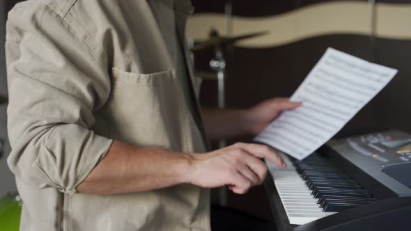 Young Man Checks Music Sheet and Plays Notes on Synthesizer