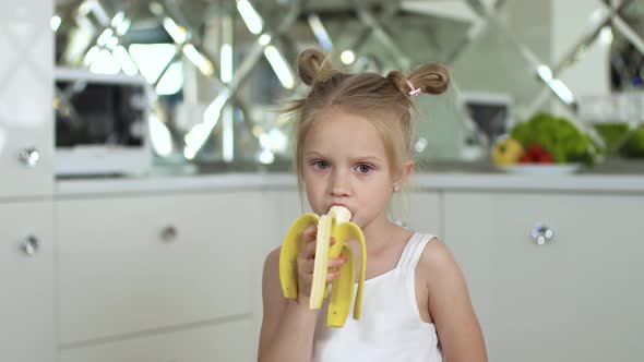 Child Eating Food. Little Girl Eating Banana At Kitchen