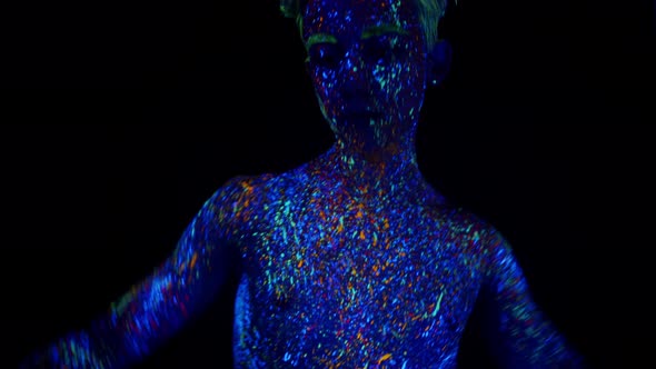 Man Covered with Phosphor Paint Dances Under Ultraviolet Light in Studio on Dark Background Front