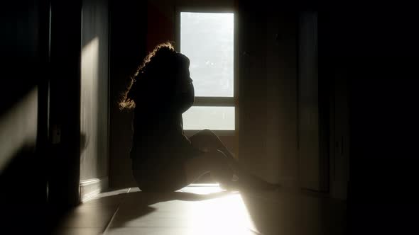 Silhouette of Frustrated Woman with Long Hair Sitting in Corridor at Sunrise or Sunset