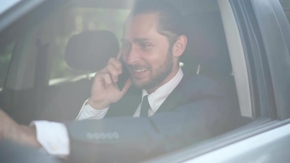 Zoom in to Happy Young Man Sitting on Driver's Seat in Sunrays Talking on Phone Smiling