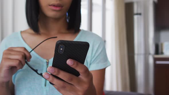 Mixed race gender fluid person standing and using smartphone at home