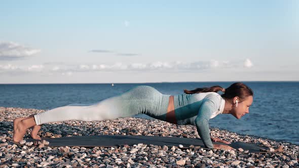 Muscular Fitness Lady Doing Push Ups on Pebble Seaside at Sunset Enjoying Outdoor Physical Activity