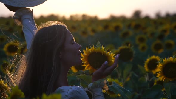 Young Woman with Long Hair and Straw Hat in a Beautiful Field of Sunflowers at Sunset Time