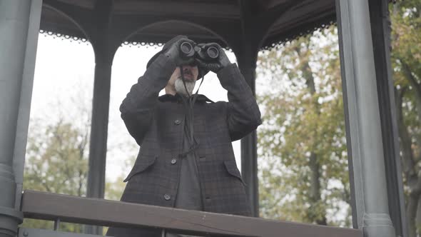 Middle Shot of Confident Bearded Caucasian Man in Leather Gloves Looking Away Using Binoculars