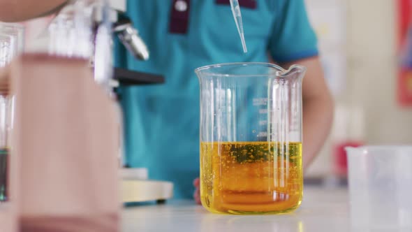 Boy wearing face mask and protective glasses using pipette and beakers in laboratory