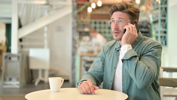 Cheerful Middle Aged Man Talking on Smartphone in Cafe 