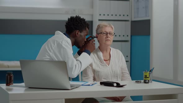 Young Doctor Using Otoscope for Ear Checkup in Cabinet