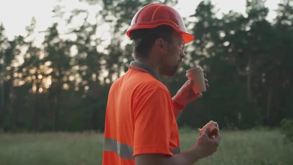 Engineer Having Lunch Near Power Lines and Electricity Pylons in the Field