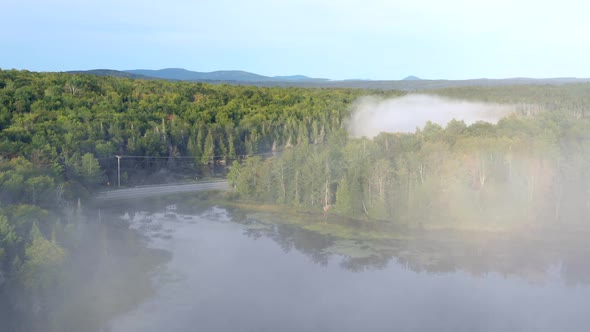 Aerial drone shot emerging from thick fog and mist to reveal the blue waters of Spectacle Pond and a