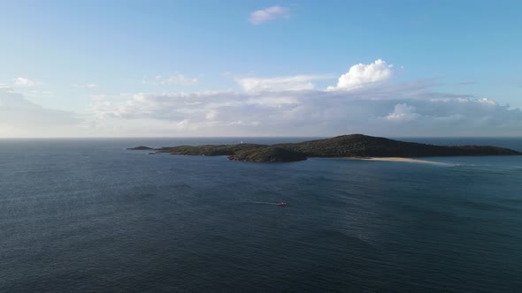 Revealing view over water of a lush vegetated Island rising above the ocean with a cloud formation i