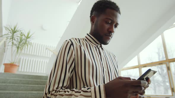 Black Man Standing on Stairs and Texting on Smartphone