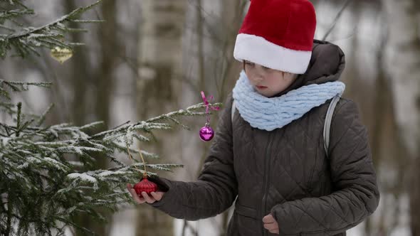 Little School Girl Is Playing with Christmas Decorations for Tree in Park at Winter Vacation