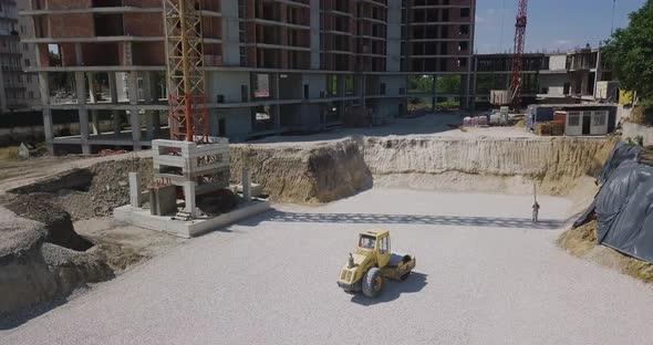 Image From Above on a Construction Site Where a Yellow Tractor Levels and Compacts the New Asphalt