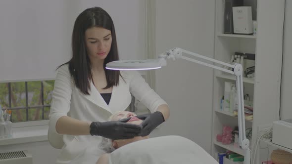 A Woman in a Beauty Salon Applies a Moisturizing Tissue Mask to Her Face