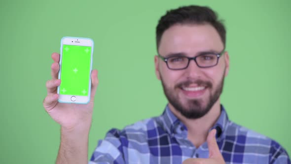 Face of Happy Young Bearded Hipster Man Showing Phone and Giving Thumbs Up