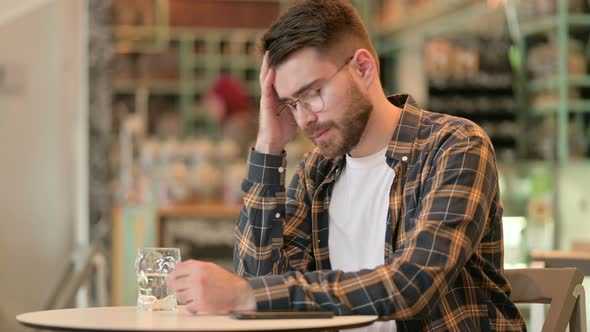 Worried Young Man with Headache Sitting in Cafe 