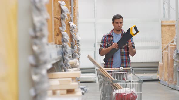 Man in a Shirt in a Hardware Store with a Cart Buys a Saw