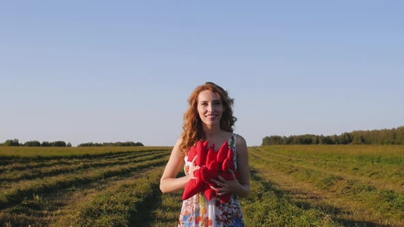 Redhead Young Woman in White Dress Throws Soft Hearts on Background of the Field