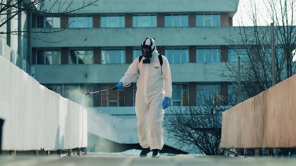 Expert in a Hazmat Suit Is Disinfecting Concrete Walls in the Street