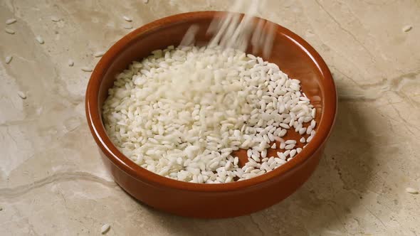 Scattering raw carnaroli risotto rice in a brown bowl close up