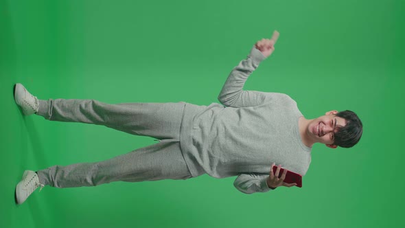 Full Body Of Man Flipping Through The Mobile Phone With A Smile Pointing To The Side On Green Screen