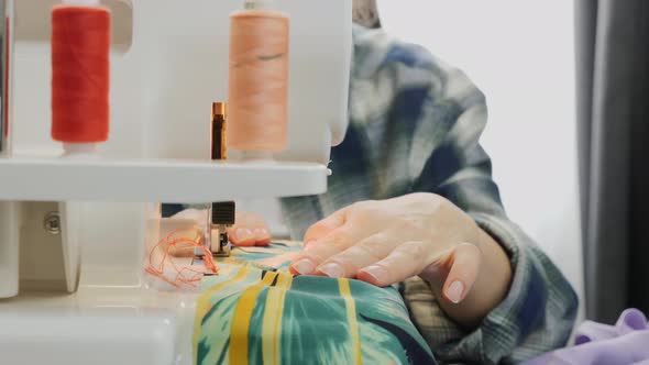 Close up of woman's hands works on overlock at sewing fabric.