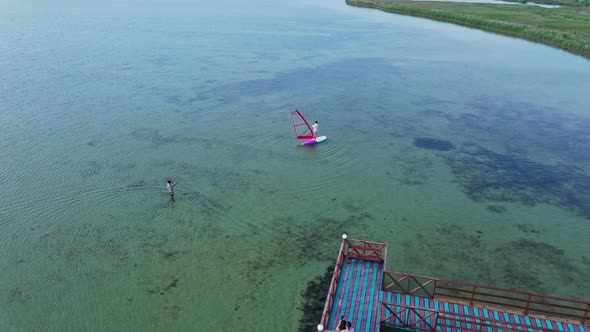 Aerial Drone Footage of Windsurf Instructor Teaching Woman Beginner To Standing on Surfboard