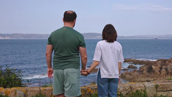 A Guy and a Girl Hold Hands and Look at the Ocean