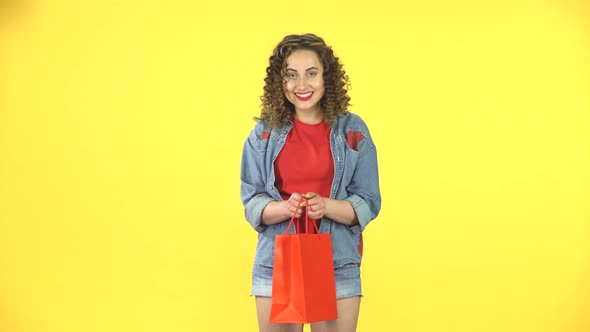 Girl Looks in the Red Package Then Surprised and Very Rejoicing on Yellow Background