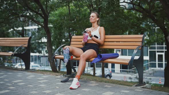 Young Girl with Prosthesis Drinking Water Sitting on Bench in Park