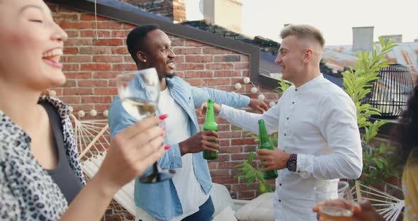 Two Multiracial Men which Drinking Beer and Talking Near His Female Friends