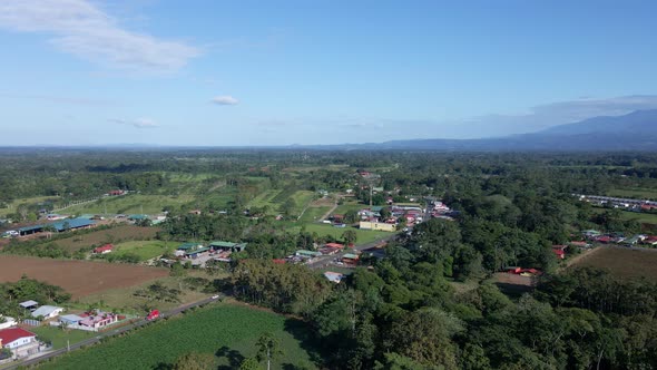 Drone footage of approaching flight toward a small central American town with vehicles driving out o